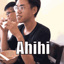 a man wearing glasses sits at a table with a bowl of food and the word ahihi written on his shirt