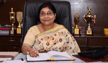 a woman is sitting at a desk with a pen in her hand in front of trophies .