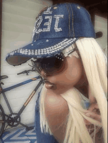 a woman wearing a denim hat and sunglasses is standing next to a bicycle .