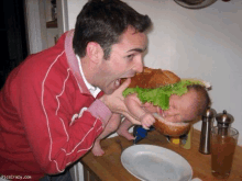 a man is holding a baby in a hamburger bun with lettuce on it ..