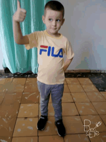 a young boy wearing a yellow fila t-shirt gives a thumbs up