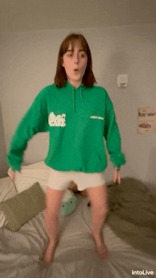 a girl wearing a green sweatshirt that says " lonely week " is jumping on a bed