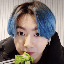 a young man with blue hair is eating a salad with chopsticks .