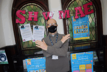 a man wearing a face mask stands in front of a sign that says shaw mae