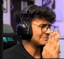 a man wearing headphones and glasses is praying while sitting in a chair .