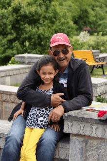 a man wearing sunglasses and a red puma hat holds a little girl