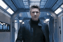 a man in a black jacket is walking down a hallway in a spaceship .