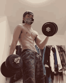 a shirtless man wearing a bandana holds a pair of dumbbells in his hands