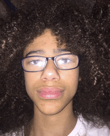 a young boy with curly hair wearing glasses and a white shirt