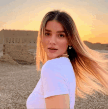 a woman in a white shirt is standing in front of a building with her hair blowing in the wind