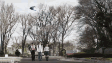 a group of people walking in a park with a kite flying in the sky with the letter t on it