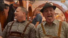 two men wearing plaid shirts and suspenders are sitting next to each other and one of them is sticking out his tongue