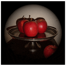 three red apples on a silver plate with shadows on the wall