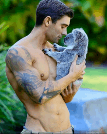 a shirtless man holds a small koala bear