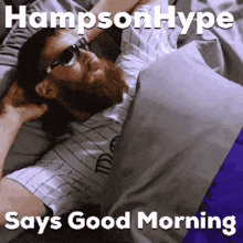 a man with a beard wearing sunglasses is laying in bed with the caption hampson hype says good morning