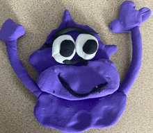 a purple stuffed animal with white eyes and a smile on its face