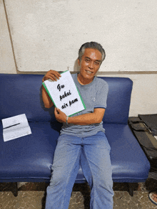 a man sitting on a blue couch holding a piece of paper that says " gu pakai air pam "