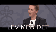 a woman in a suit stands in front of a microphone with lev med det written in white letters