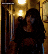 a woman in a black shirt is standing in a dark hallway looking at the camera .