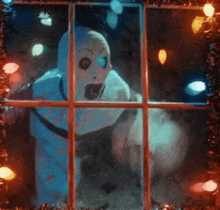 a snowman is looking out a window with christmas lights in the background