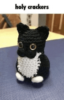 a black and white crocheted cat is sitting on top of a blue table .