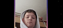 a young boy wearing a white hoodie looks at the camera with his eyes closed