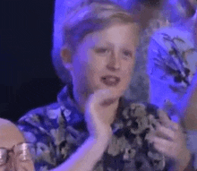 a young boy is clapping his hands while sitting in a crowd .