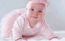 a baby girl wearing a pink tutu and headband is crawling on the floor .