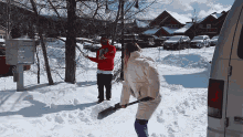 a man in a red sweatshirt with the letter s on it is standing next to a woman shoveling snow