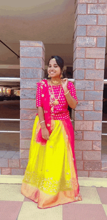 a woman wearing a pink top and yellow skirt is standing in front of a brick wall