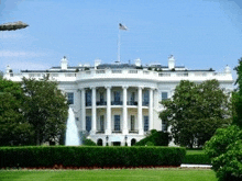 a white house with a fountain in front of it and a plane flying in the sky .