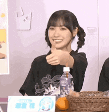 a woman is giving a thumbs up sign while sitting at a table with a bottle of water and an orange .