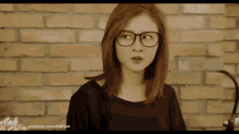 a woman wearing glasses and a black shirt is standing in front of a brick wall .