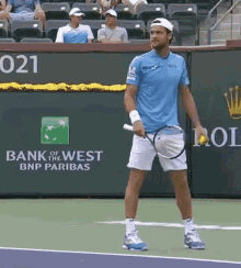 a man holding a tennis racquet on a tennis court with a bank of west bnp paribas sign behind him