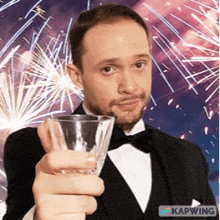 a man in a tuxedo is holding a glass in front of fireworks ..