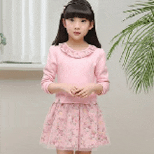 a little girl is standing in front of a window wearing a pink sweater and a pink skirt .