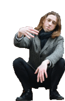 a man with long hair is squatting down with his hands in his pockets