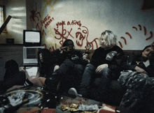 a group of people sitting on a couch with graffiti on the wall saying " hate mom "