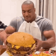 a muscular man is eating a very large hamburger and french fries