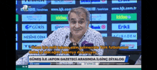 a man is talking into a microphone in front of a screen that says ' günes ile japon gazeteci '