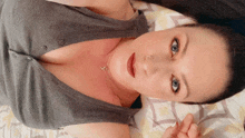 a woman in a grey tank top is laying on a bed and looking at the camera .