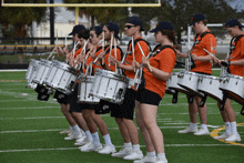 a marching band is playing drums on a field and they are wearing orange shirts that say ucsd