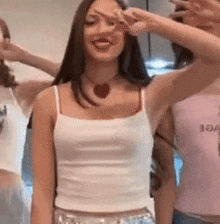 a woman in a white tank top is making a peace sign while standing next to two other women .