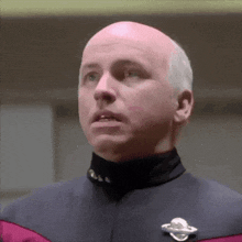 a bald man wearing a uniform with a planet pin on his jacket