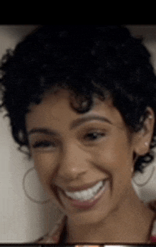 a close up of a woman 's face with curly hair and hoop earrings smiling .