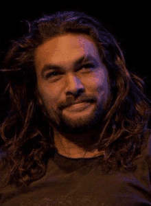 a man with long hair and a beard is smiling in a dark room .