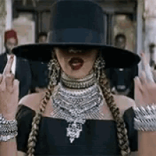 a woman wearing a hat , necklace , bracelets and braids is giving the middle finger .