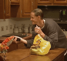 a man in a kitchen holds a bag of chips that says ' chicken ' on it