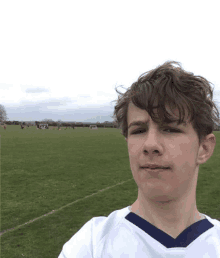 a young boy in a white shirt with a blue v-neck is standing in a field