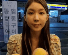 a woman in a floral shirt is holding two oranges in front of a store with chinese writing on it